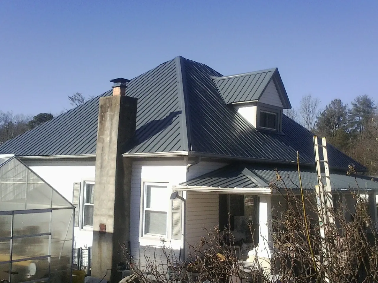 Dark blue standing seam metal roof on a white farmhouse with dormer — Slate & Tile Roof Repair by Roofing Brothers in Alburtis