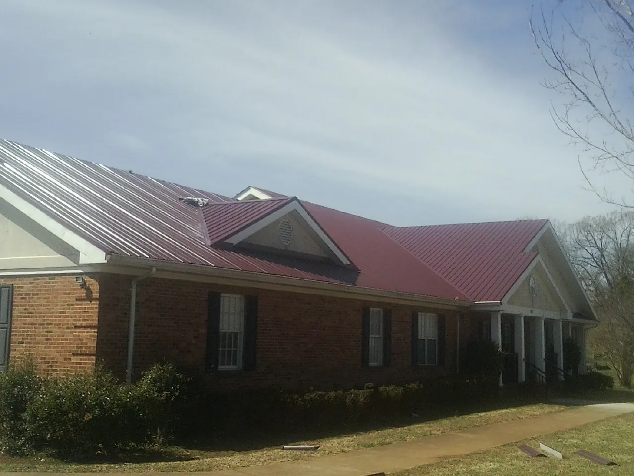 Red metal roof with gabled entries on a long brick building, from a Hail Damage Roof Repair job in Alburtis