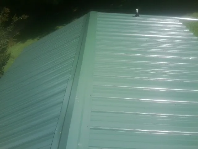 New green metal panels meeting at the ridge of a roof — Flat Roof Repair work by our crew in Alburtis