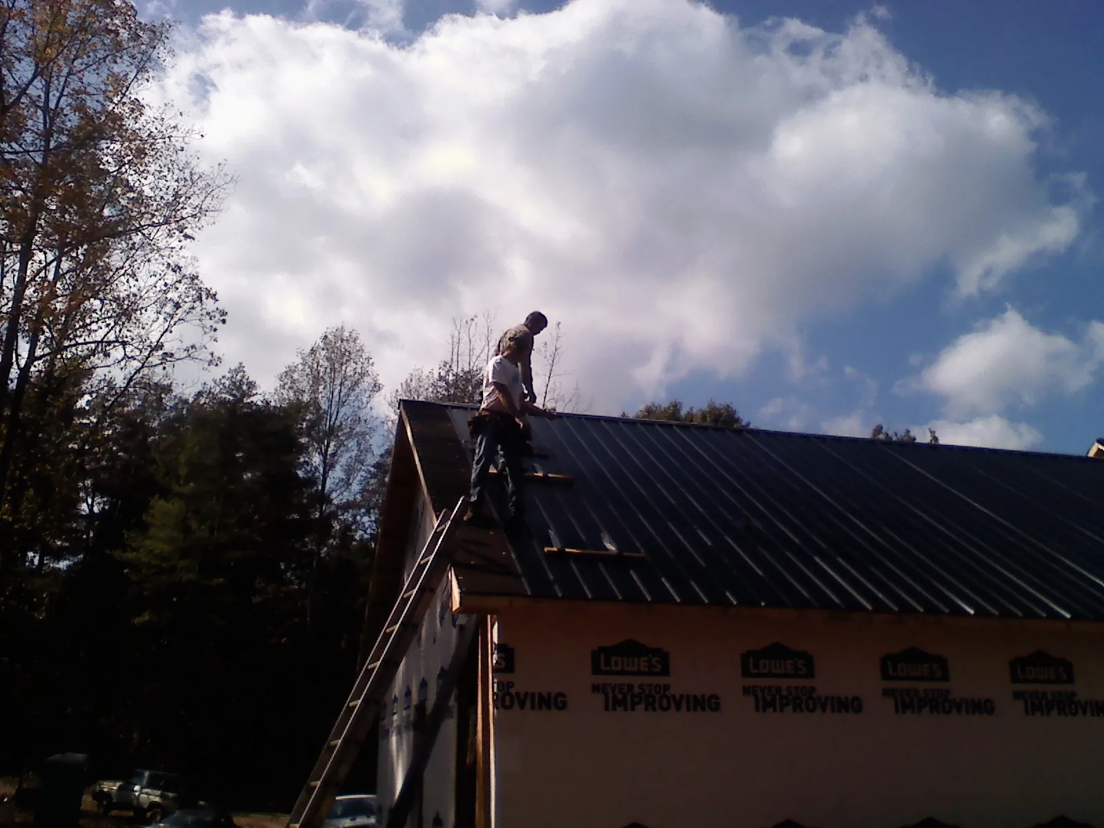 Roofer fastening dark metal panels high against a cloudy sky, from a Roof Inspection job in Alburtis