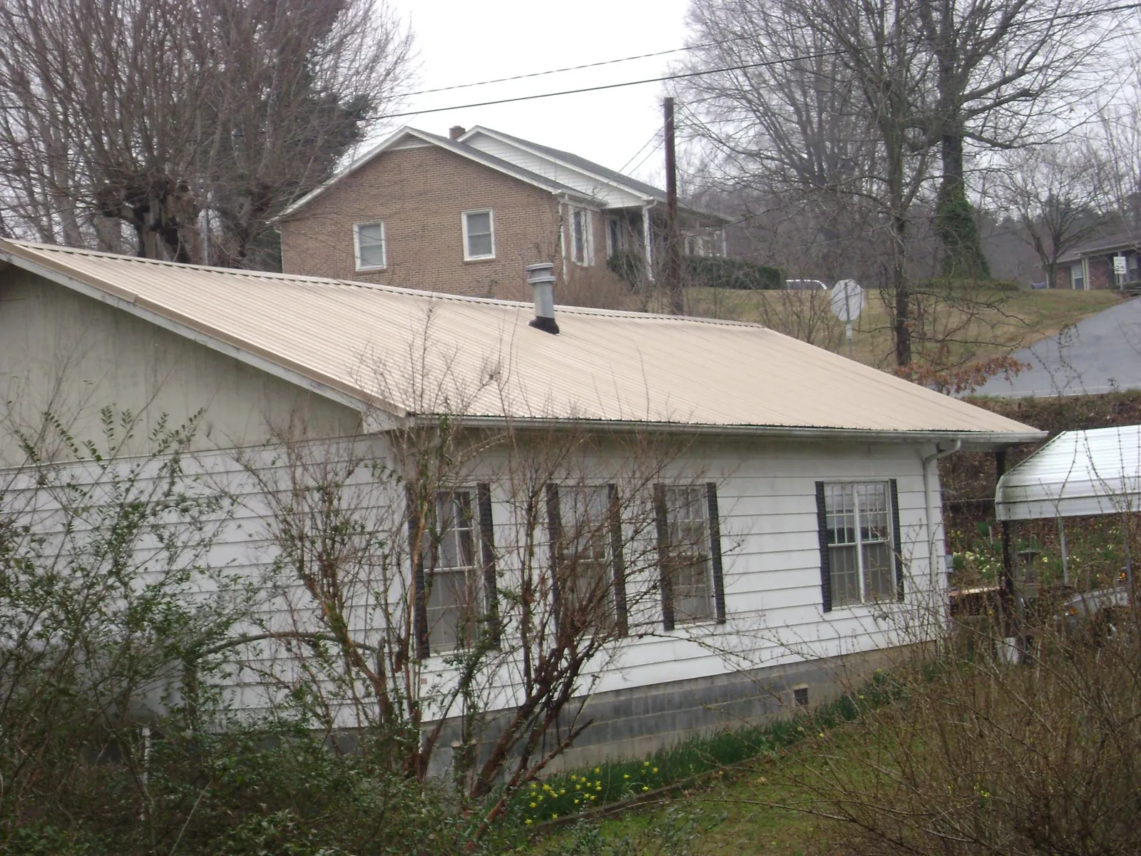 Tan metal roof on a white sided house set into a hillside — Commercial Roofing by Roofing Brothers in Alburtis
